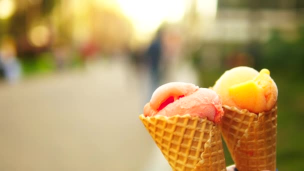 有人把水果冰淇淋放在晶圆锥里，特写。在春天或夏天对一个模糊的步行街 — 图库视频影像