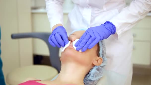 Begreppet kosmetolog. kosmetolog applicerar lotion med bomullspinne på kvinnan ansikte. hudrengöring — Stockvideo