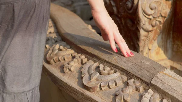 Primer plano. la mano de las mujeres se desliza sobre una barandilla tallada en madera en un templo budista de madera — Foto de Stock