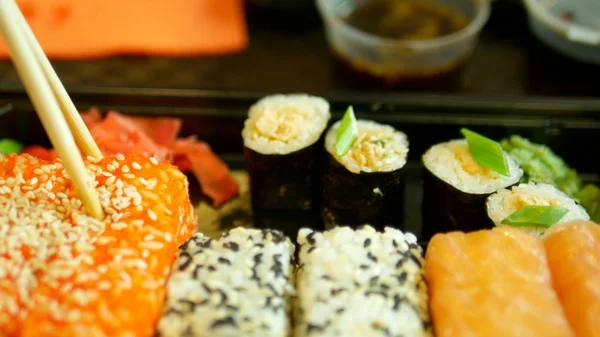 Close-up. alguém leva sushi com pauzinhos, rolos e mergulhos em molho de soja — Fotografia de Stock