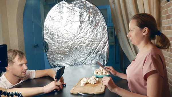 cooking courses online. cooking and culinary classroom training concept. a female blogger prepares mushrooms in the kitchen and shoots a video about herself using a mobile phone on a tripod.