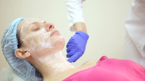 The concept of a beautician. Beautician puts the cream on the girls face — Stock Video