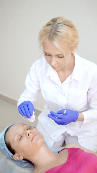 O cosmetologista faz injeções, procedimentos anti-envelhecimento para apertar e alisar rugas na pele do rosto e pescoço de uma mulher. verticalmente — Vídeo de Stock