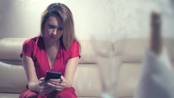 Uma mulher chorando está esperando por alguém em casa em um conjunto de mesa para um encontro romântico para dois. verifica o telefone — Vídeo de Stock