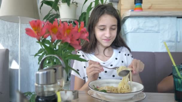 Tiener meisje met lange zwarte haren eet spaghetti in een restaurant met een vork en lepel — Stockvideo