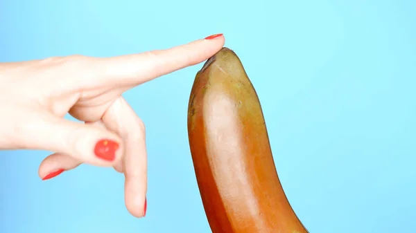 Female hands with a red manicure touch a red banana on a blue background — Stock Photo, Image