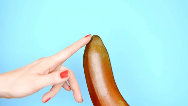 As mãos femininas com uma manicura vermelha tocam uma banana vermelha em um fundo azul — Fotografia de Stock