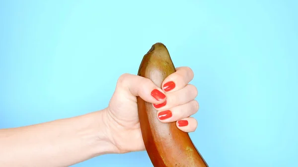Kvinnliga händer med en röd manikyr touch en röd banan på en blå bakgrund — Stockfoto
