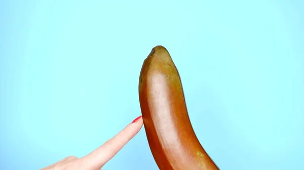 Female hands with a red manicure touch a red banana on a blue background — Stock Photo, Image