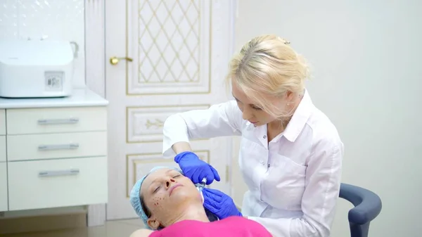 The cosmetologist makes injections, anti-aging procedures for tightening and smoothing wrinkles on the skin of the face and neck of a woman.