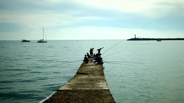 Siluetas de pescadores sentados en el viejo muelle. pesca junto al mar en un día soleado brillante — Foto de Stock