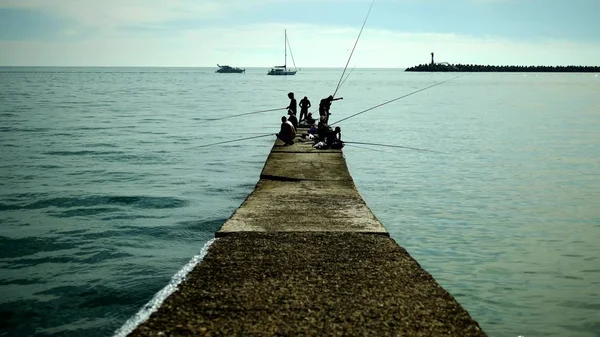 Silhuetas de pescadores sentados no velho cais. pesca junto ao mar em um dia ensolarado brilhante — Fotografia de Stock
