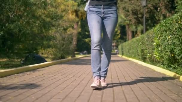 Женские ноги в джинсах и кроссовках на мощеной дорожке — стоковое видео