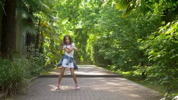 Hermosa chica delgada adolescente con pelo largo y oscuro bailando en el parque de verano entre el verde — Vídeos de Stock