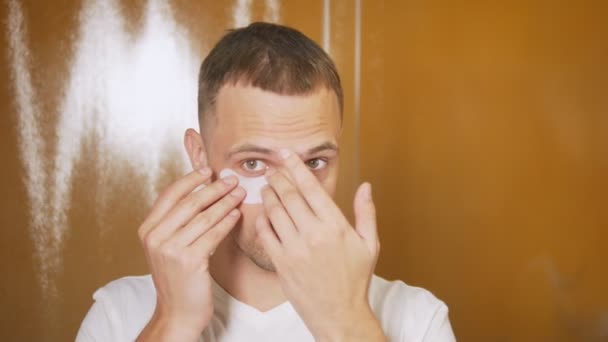 Portrait d'un bel homme avec un masque sous les paupières, dans la salle de bain. Concept métrosexuel, soins du visage — Video