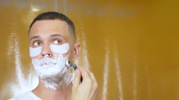 Portret van een knappe man met oogmasker, die scheert met een scheermesje in de badkamer. Metrosexual concept — Stockvideo