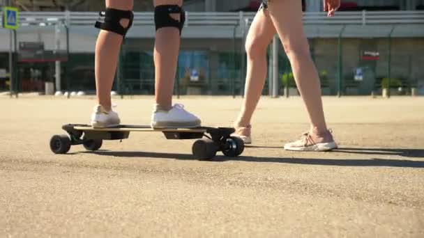 Flicka som rider på en elektrisk skateboard. närbild, kvinnliga ben. ett par flickor som går i parken, en flicka på en elektrisk skateboard, den andra promenader bredvid, håller hennes hand — Stockvideo