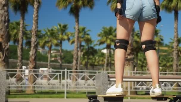 Menina montando um skate elétrico em um belo parque com palmeiras altas — Vídeo de Stock
