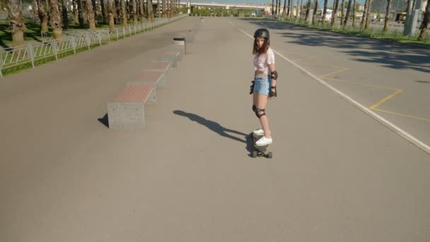 Girl riding an electric skateboard in a beautiful park with tall palm trees — Stock Video