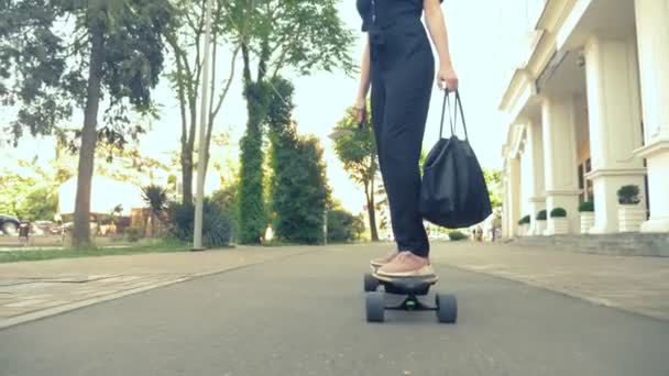 Uma mulher de negócios moderna em um macacão preto em tênis rosa, óculos de sol e um saco preto, montando um quadro elétrico ao longo de uma rua da cidade. O conceito de aventuras estranhas de pessoas — Vídeo de Stock