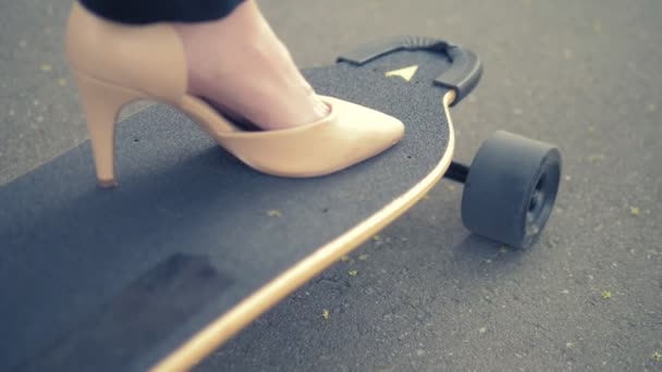 Primer plano. zapato beige para mujer en una tabla de skate negro. Mujer de negocios moderna en zapatos beige bombas, paseos en un tablero eléctrico a lo largo de una calle de la ciudad. El concepto de lograr la meta y el liderazgo — Vídeo de stock