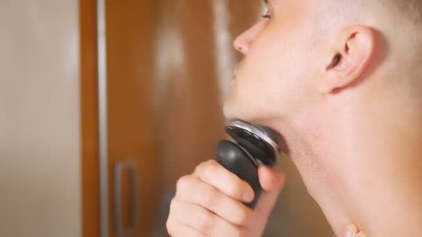 Retrato de un hombre guapo con una máscara de ojos que se afeita con una navaja eléctrica en el baño. Concepto metrosexual — Vídeo de stock