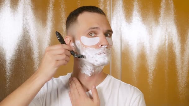 Portret van een knappe man met oogmasker, die scheert met een scheermesje in de badkamer. Metrosexual concept — Stockvideo