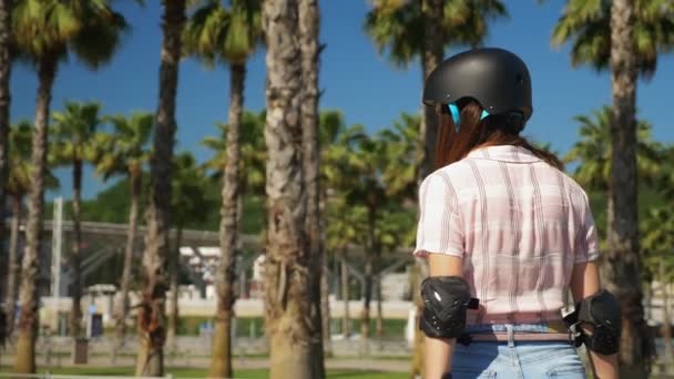 Menina montando um skate elétrico em um belo parque com palmeiras altas — Vídeo de Stock