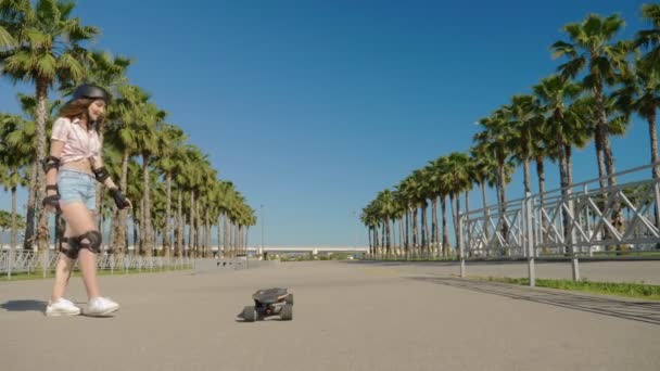 Flicka rider en elektrisk skateboard i en vacker park med höga palmer — Stockvideo