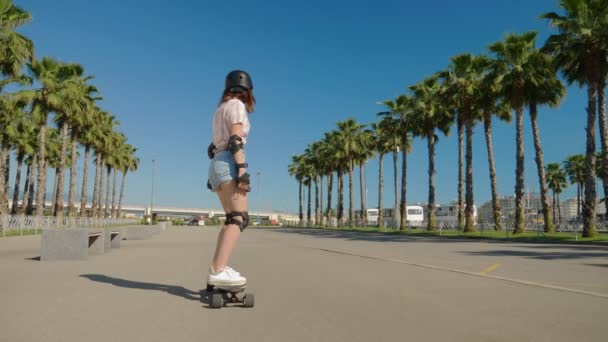 Дівчина їде на електричному скейті в красивому парку з високими пальмами — стокове відео