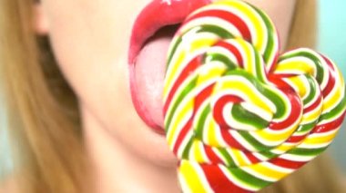 yakın çekim, kırmızı ruj ile kadın dudaklar, yemek ve bir kalp şeklinde büyük bir lolipop yalamak.