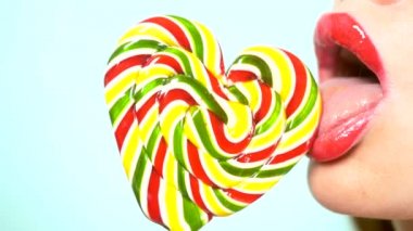 yakın çekim, kırmızı ruj ile kadın dudaklar, yemek ve bir kalp şeklinde büyük bir lolipop yalamak. kopya alanı, mavi arka plan