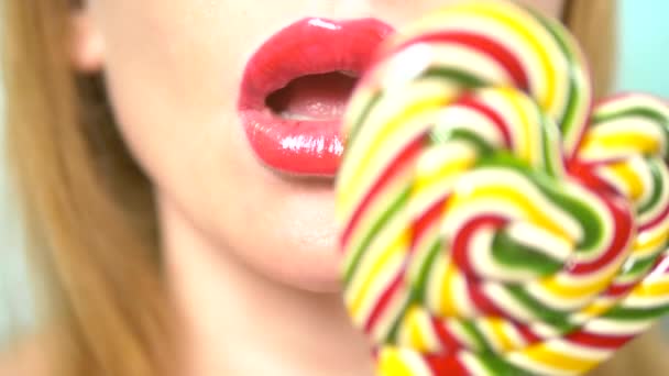 クローズアップ、赤い口紅を持つ女性の唇は、食べて、心臓の形で大きなロリポップを舐める. — ストック動画