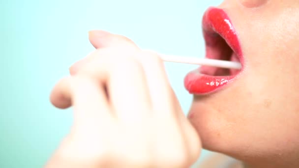 빨간 립스틱으로 클로즈업, 여성 섹시한 입술은 큰 핑크 라운드 롤리팝을 빨아. 복사 공간. 파란색 배경 — 비디오