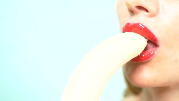 クローズ アップ。バナナを食べる美しい赤いメイクで美しい女性のセクシーな唇。スペースをコピーします。青い背景. — ストック動画