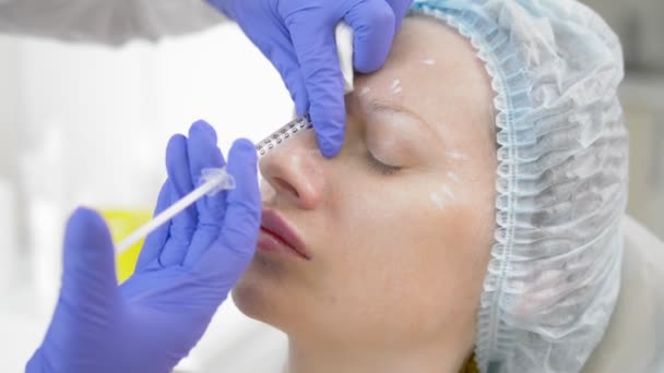 Z tworzywa sztucznego. Kosmetolog wstrzykuje toksyny botulinowej, aby dokręcić i wygładzić zmarszczki na skórze kobiecej twarzy. — Wideo stockowe