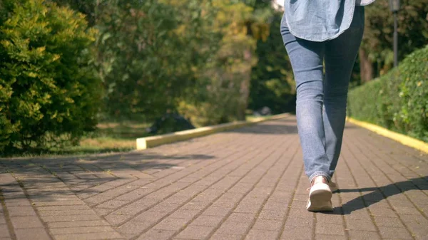 Wanita kaki dalam celana jeans dan sepatu berada di jalan beraspal — Stok Foto
