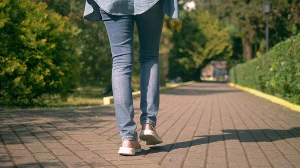 A női lábak farmerban és tornacipőben egy kövezett úton vannak. — Stock Fotó