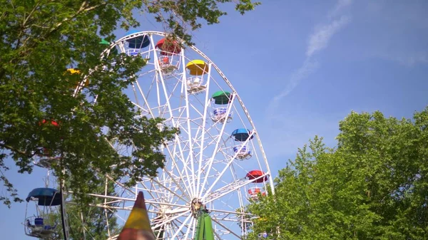 Красочное колесо обозрения на фоне голубого неба и зеленых деревьев — стоковое фото