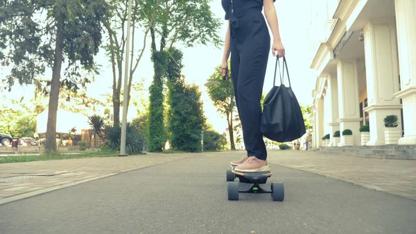 Pembe spor ayakkabı, güneş gözlüğü ve siyah bir çanta siyah tulum içinde modern bir iş kadını, bir şehir sokak boyunca bir elektrik tahtası sürme. Insanların garip maceralar kavramı — Stok fotoğraf