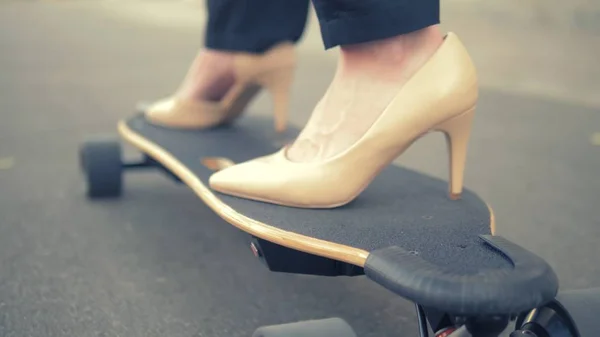 close-up. womens beige shoe on a black skate board. Modern business woman in beige pumps shoes, rides on an electric board along a city street. The concept of achieving the goal and leadership