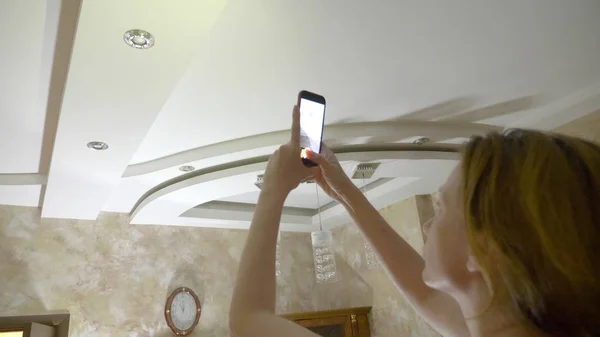 Water damage. concept of flooding the apartment and property insurance. a woman takes a photo on the phone as water drips from the ceiling of her apartment