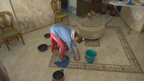 Daño al agua. Concepto de inundación del apartamento y el seguro de propiedad. gotea agua del techo en el apartamento, y una mujer limpia el agua del suelo con trapos y una fregona — Foto de Stock