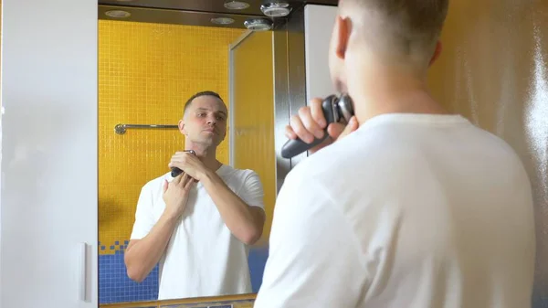 Porträtt av en vacker man med en ögonmask som rakar med en elektrisk rakhyvel i Bad rums. Metrosexual koncept — Stockfoto