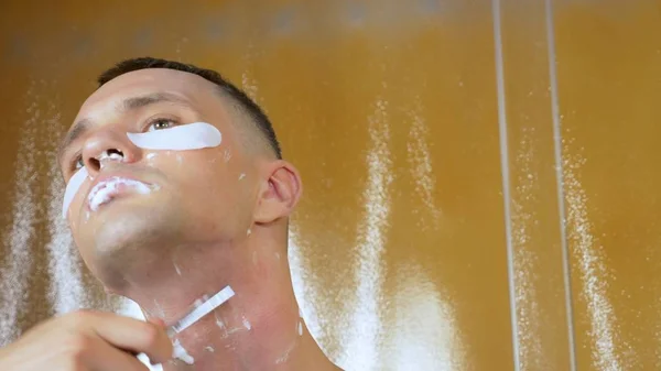一个英俊男子的画像，下眼睑下戴着面具，在浴室里用直剃须刀剃了一下。都市性概念 — 图库照片