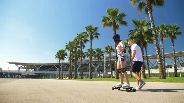 Pria mengajarkan gadis untuk naik skateboard listrik di taman dengan pohon palem tinggi — Stok Foto