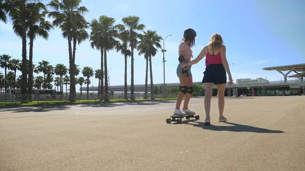 Gadis naik skateboard listrik. close-up, kaki perempuan. sepasang gadis berjalan di taman, seorang gadis di papan luncur listrik, yang lain berjalan di samping, memegang tangannya — Stok Foto