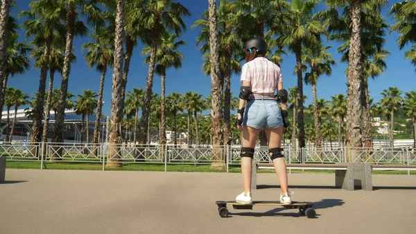 Dívka jezdila na elektrickém skateboard v krásném parku s vysokými palmami — Stock fotografie