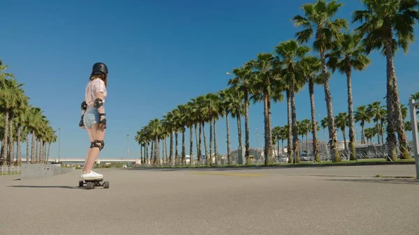 girl riding an electric skateboard in a beautiful park with tall palm trees
