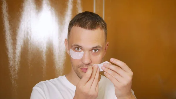 Retrato de un hombre guapo con una máscara debajo de los párpados, en el baño. Concepto metrosexual, cuidado facial —  Fotos de Stock